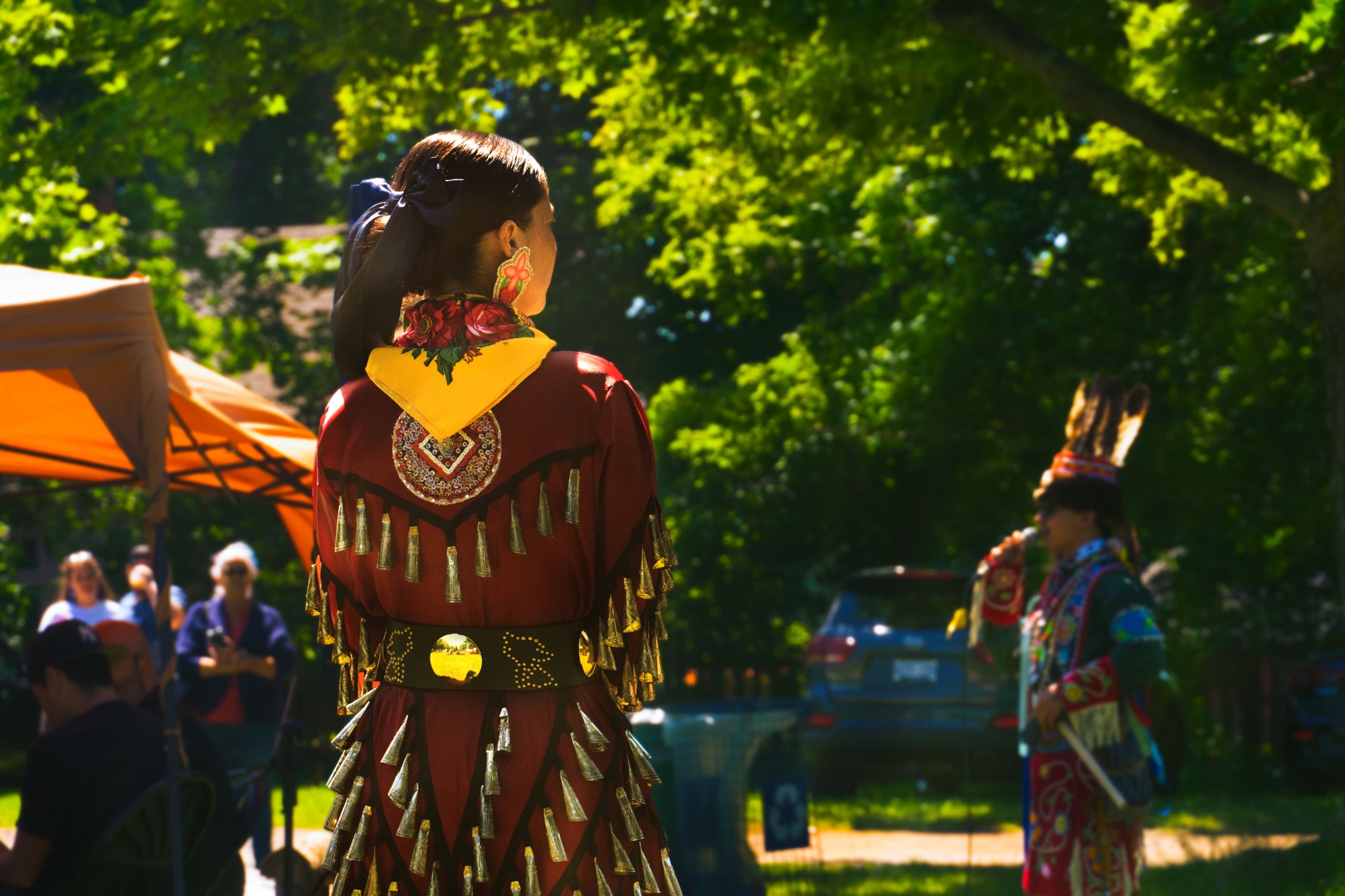 Indigenous participant in traditional regalia photographed from behind at an outdoor event